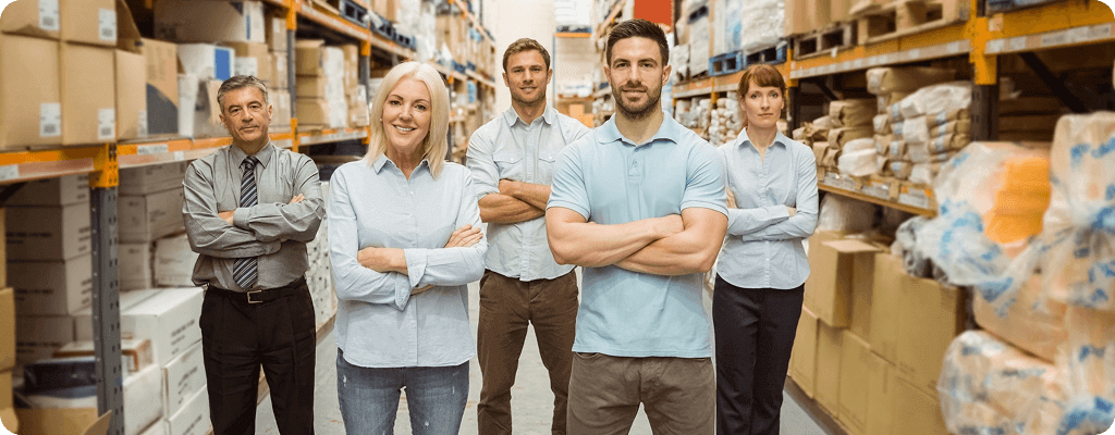 Equipo de cinco personas de pie con los brazos cruzados en el pasillo de una bodega llena de cajas