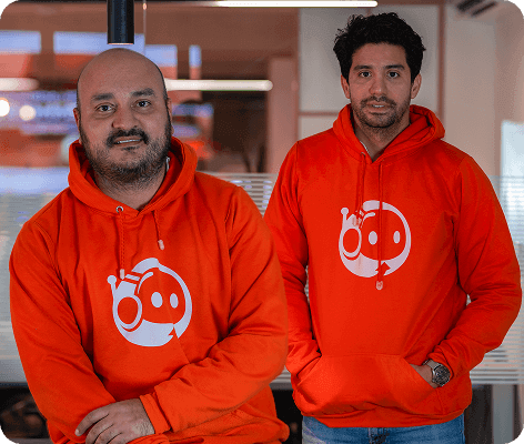 Dos hombres con buzos naranjas del logo de Dropi, de pie en una oficina